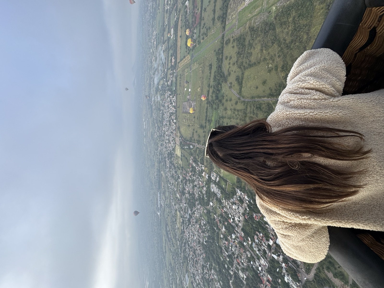 Looking over the balloon basket edge at the Teotihuacán valley dotted with hot-air balloons